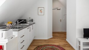 Una cucina moderna con mobili bianchi, un lavello, un tostapane e una macchina per il caffè. Si vede un quadro appeso al muro e un tappeto colorato sul pavimento.