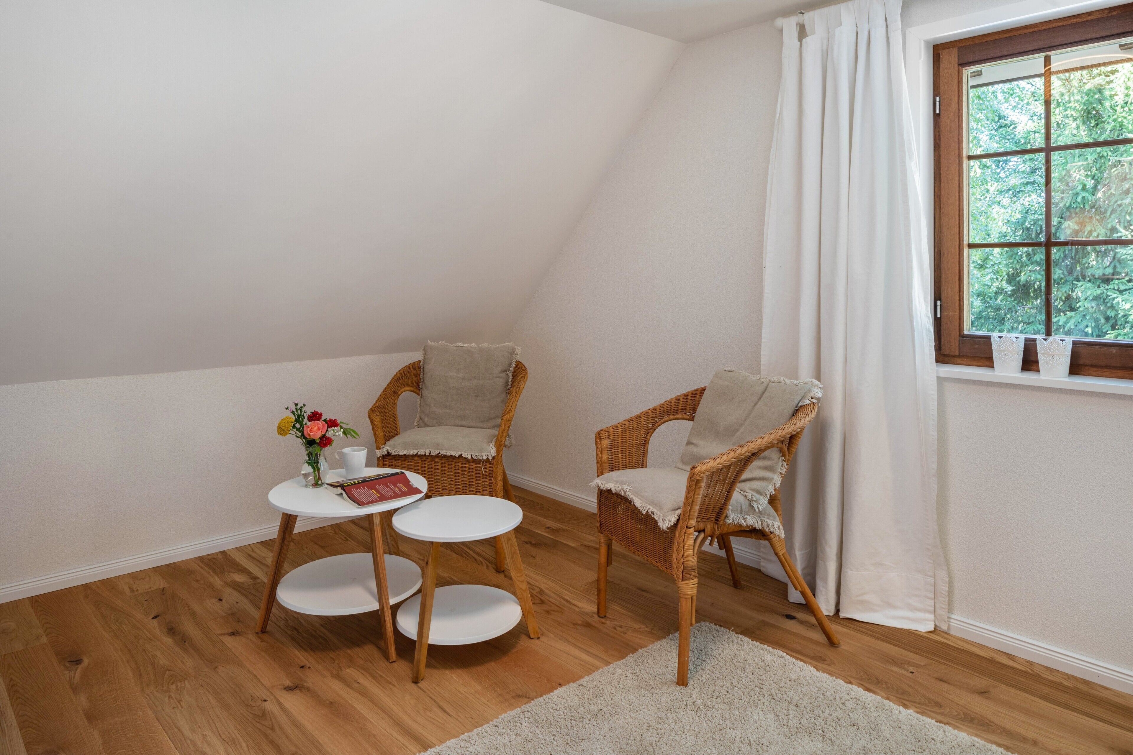 Une pièce chaleureuse avec deux fauteuils en osier, une petite table et une fenêtre avec des rideaux.