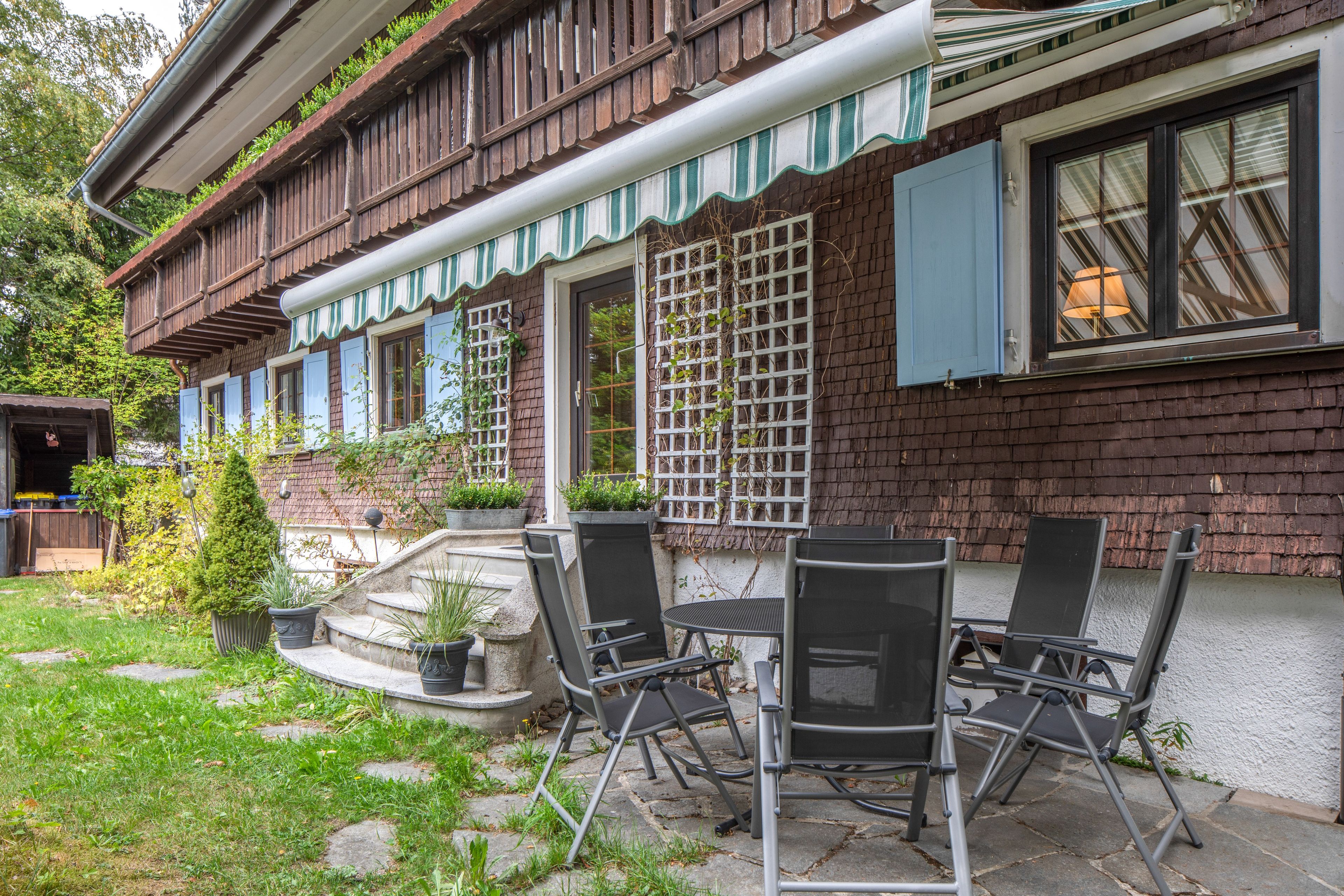 Ett traditionellt trähus med en inglasad veranda, utomhusmöbler och en trädgård.