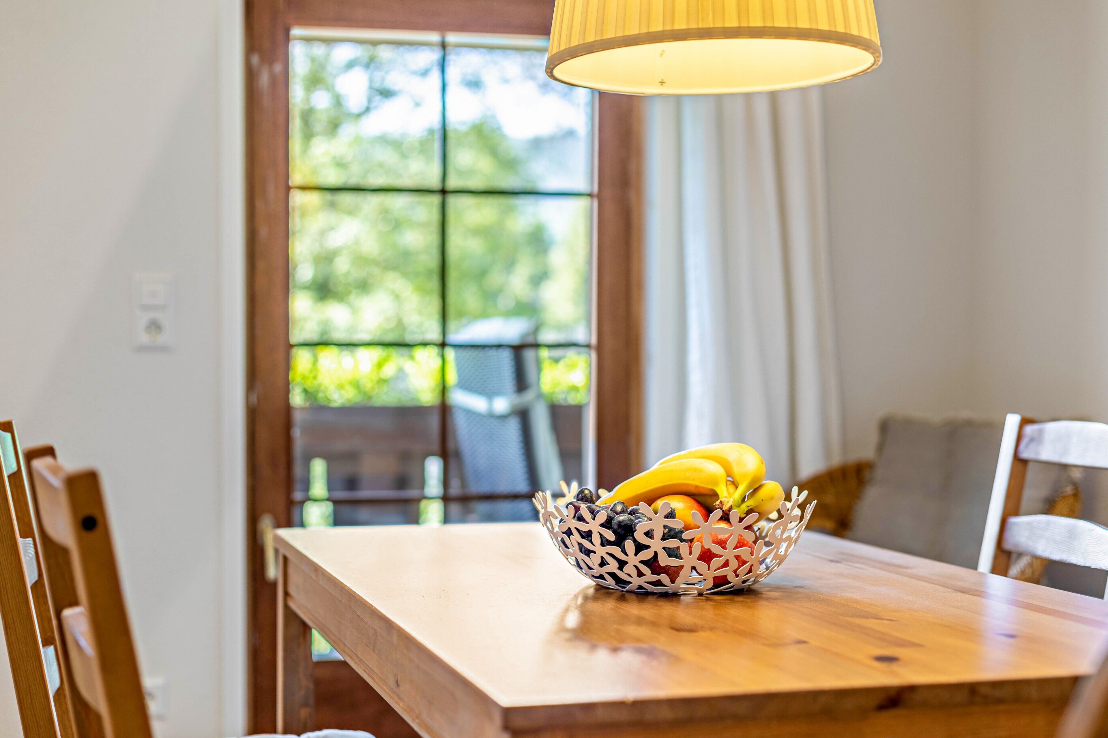 A wooden table with a fruit bowl containing bananas, apples, and berries.