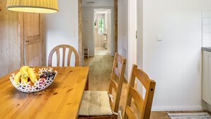 Een houten eettafel met een schaal fruit, stoelen en een gele hanglamp.