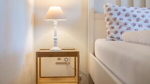 Ein Nachttisch mit Lampe, Steckdose und einem Bett mit einem Blumenkissen.