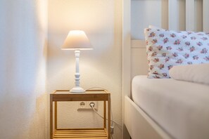 Ein Nachttisch mit Lampe, Steckdose und einem Bett mit einem Blumenkissen.