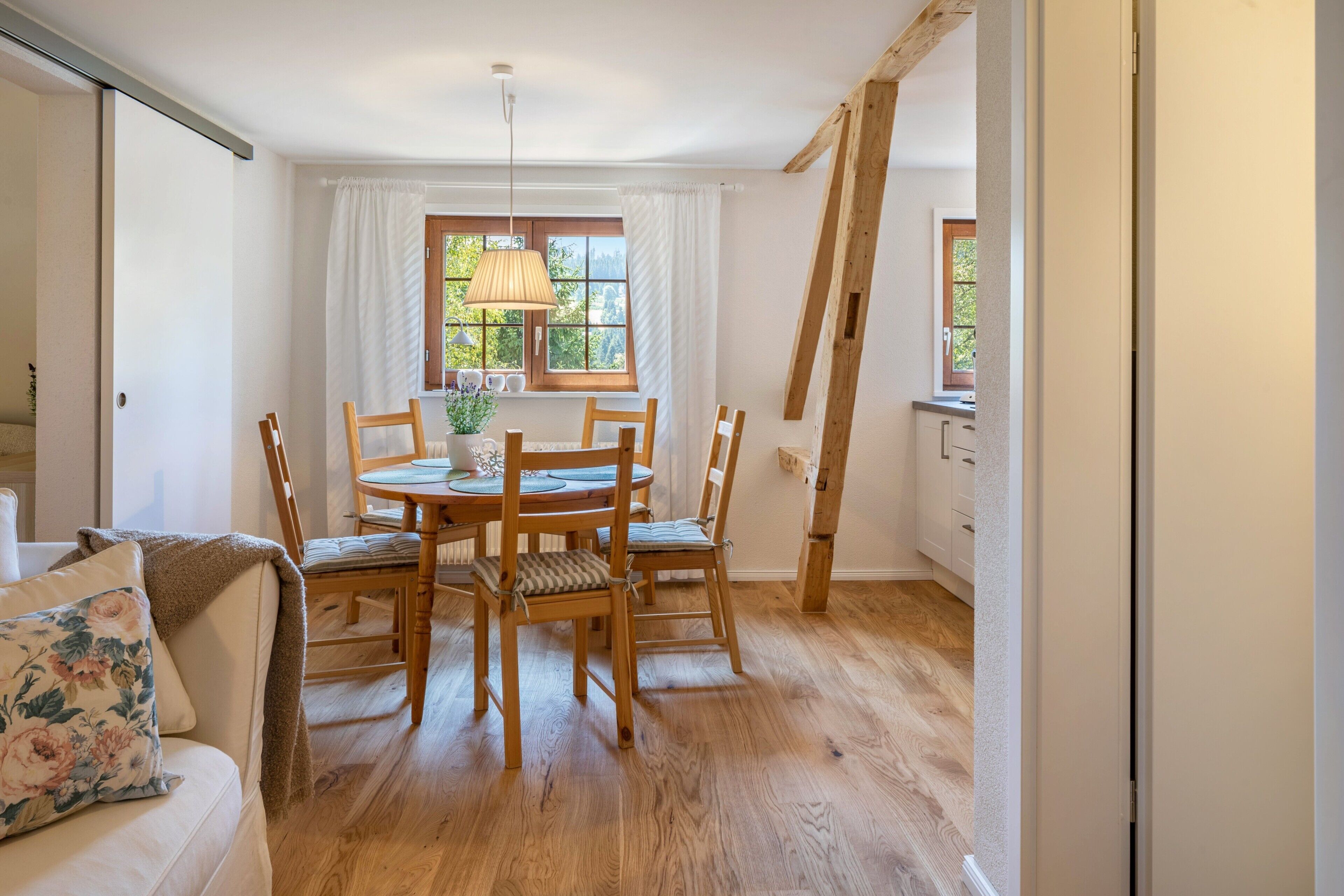 Ein Essbereich mit Holztisch und -stühlen, einer Pendelleuchte und einem Fenster mit Vorhängen.