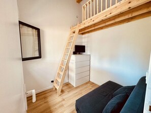 Una habitación con una escalera de madera, un aparador blanco, un sofá negro y una ventana con persianas.