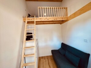 Ein Schlafzimmer im Loft-Stil mit einer Holzlade, die zu einem Etagenbett führt, einem dunklen Sofa und einem weißen Kleiderschrank.