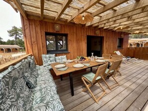 Una terraza de madera con una mesa de comedor lista para cuatro personas, rodeada de sillas de madera y un banco acolchado.