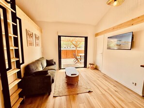 Ein Wohnzimmer mit Sofa, Couchtisch, Fernseher und Blick auf eine Terrasse.