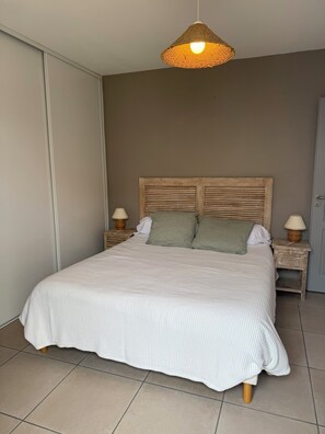 A bedroom with a bed, two bedside tables, a hanging light fixture, and a door. - Small Seaside House, Rated 3* (Saint-Denis-d'Oléron)