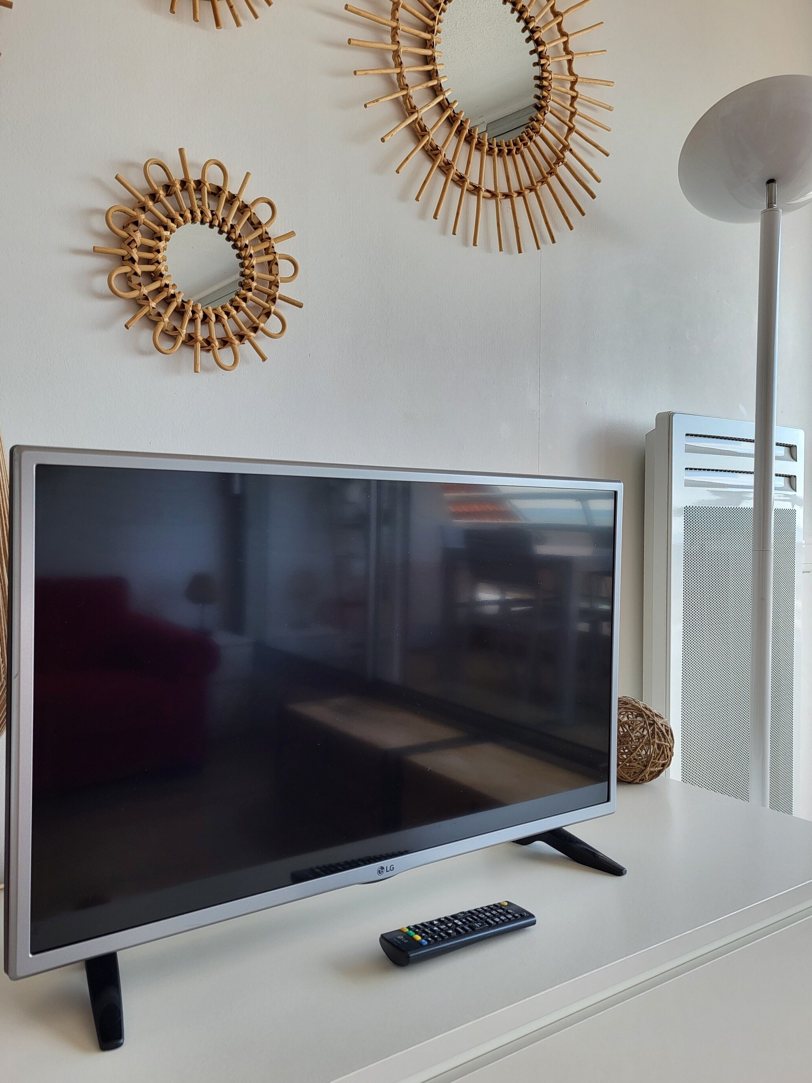 A flat-screen TV on a white stand, a remote control, and two wall decorations.