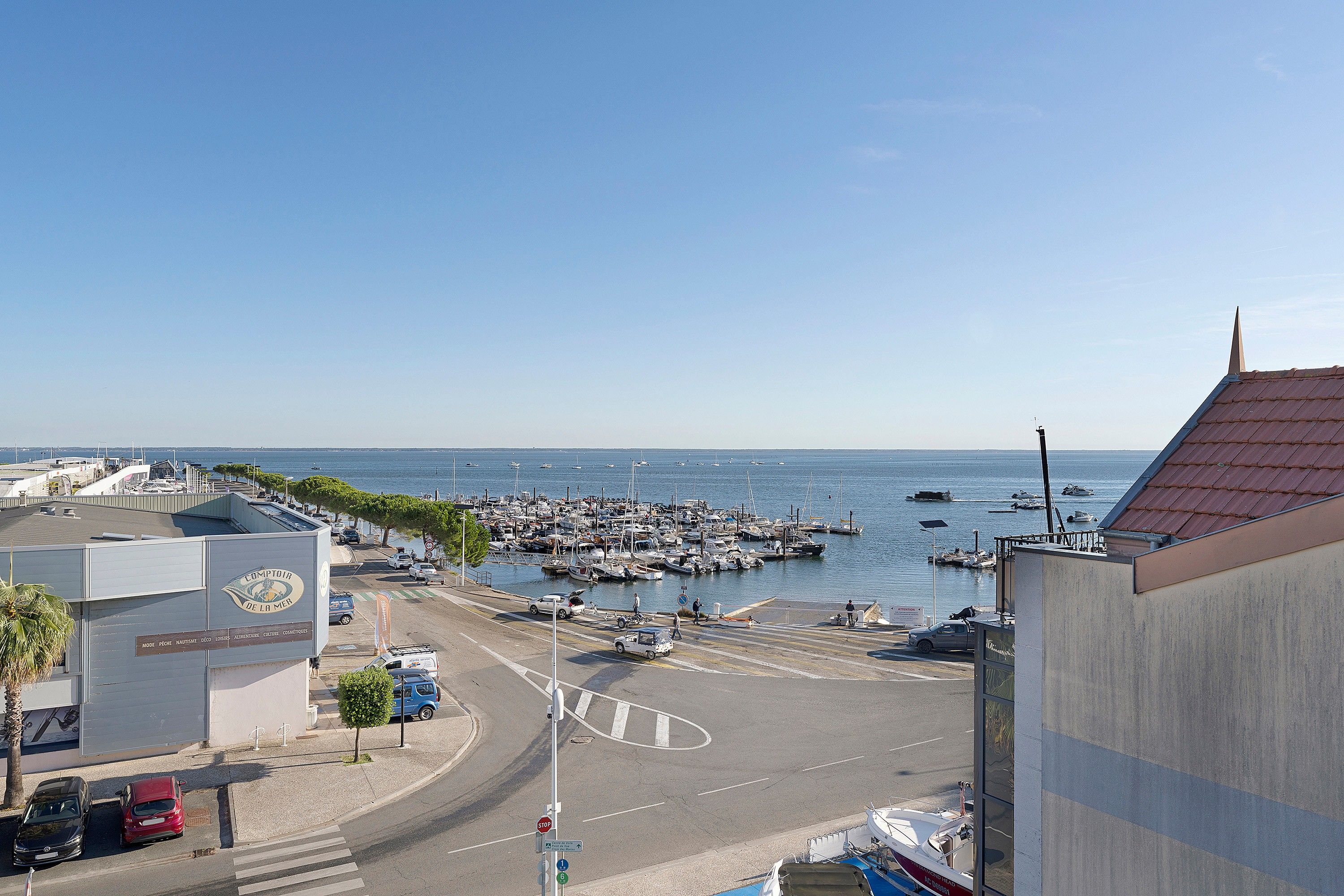 A marina with boats docked, a road with cars, and a building with a sign.