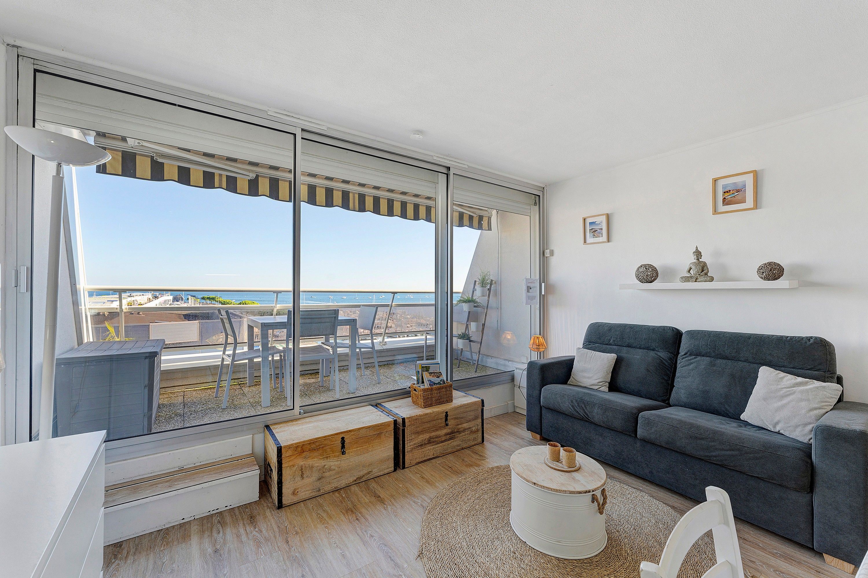 A modern living room with a large sliding glass door, a grey sofa, a small coffee table, and a view of the sea.