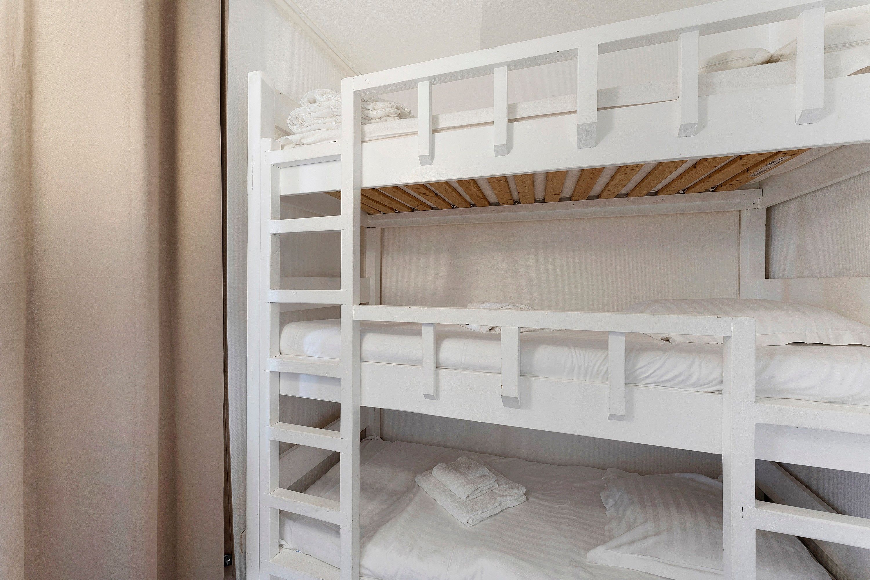 Una cama litera con escalera de madera, ropa de cama blanca y cabecera.
