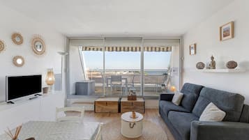 A modern living room with a balcony, a flat-screen TV, a grey sofa, and decorative wall art.
