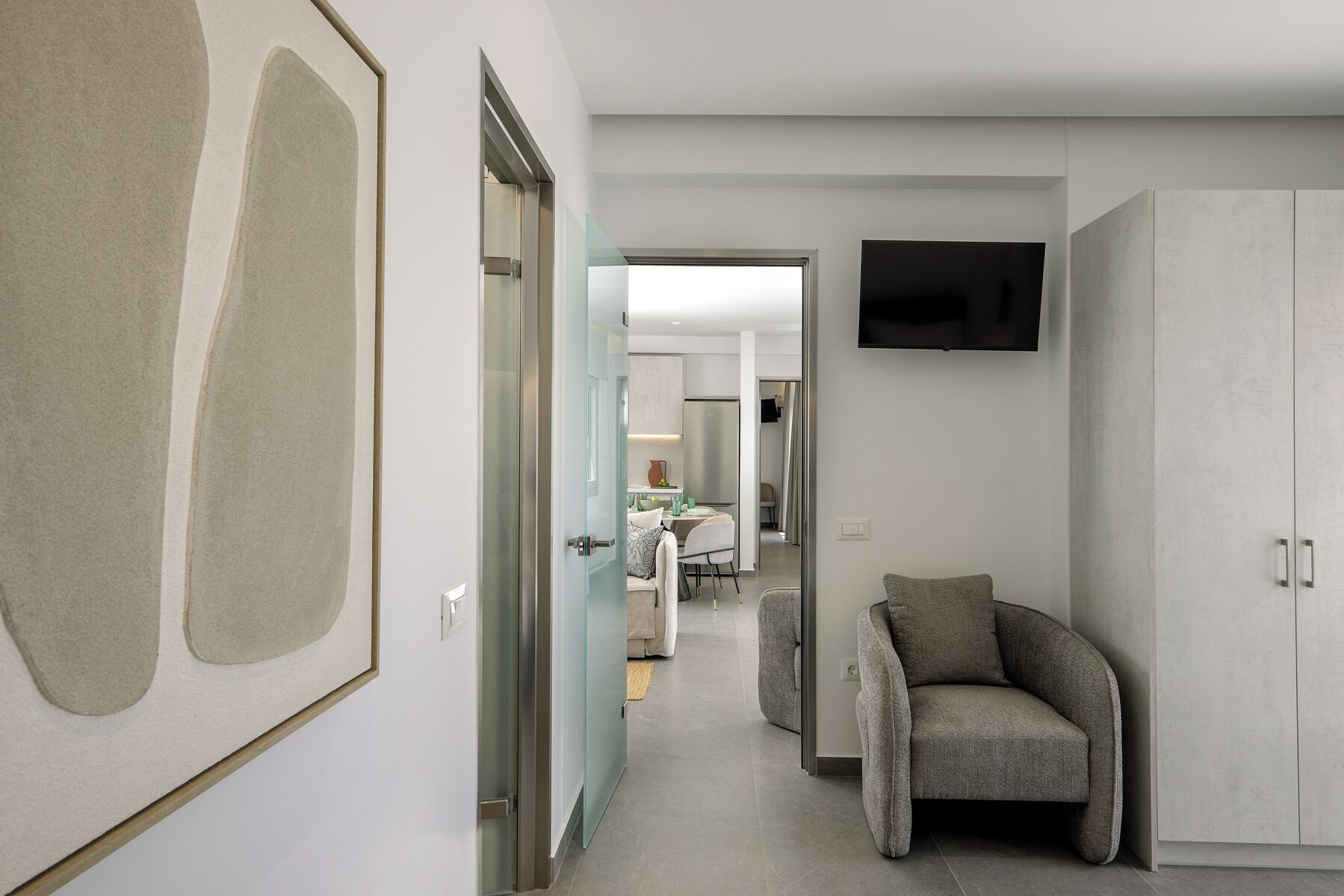 Un couloir moderne avec un canapé, un téléviseur fixé au mur et, au fond, un coin repas.