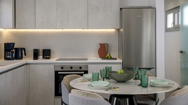 A modern kitchen with a built-in oven, a stainless steel refrigerator, and a dining area with a round table set for four. - Trinity Secret Villas (fira)