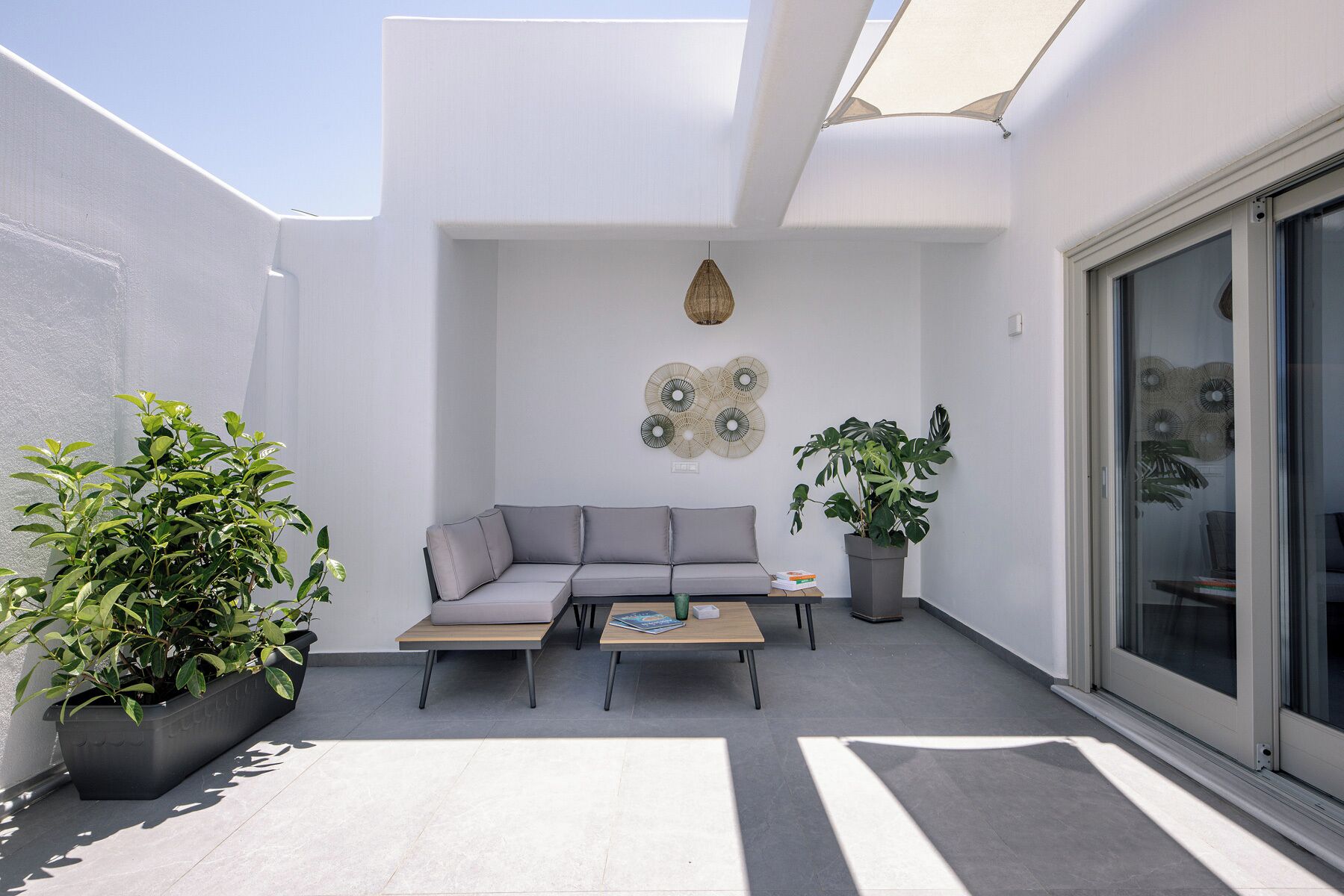Un espace de vie extérieur moderne, comprenant un canapé gris, deux tables et des plantes en pot.