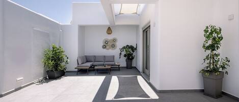 Un patio moderno al aire libre con un sofá gris, dos plantas en macetas y un adorno de pared decorativo.