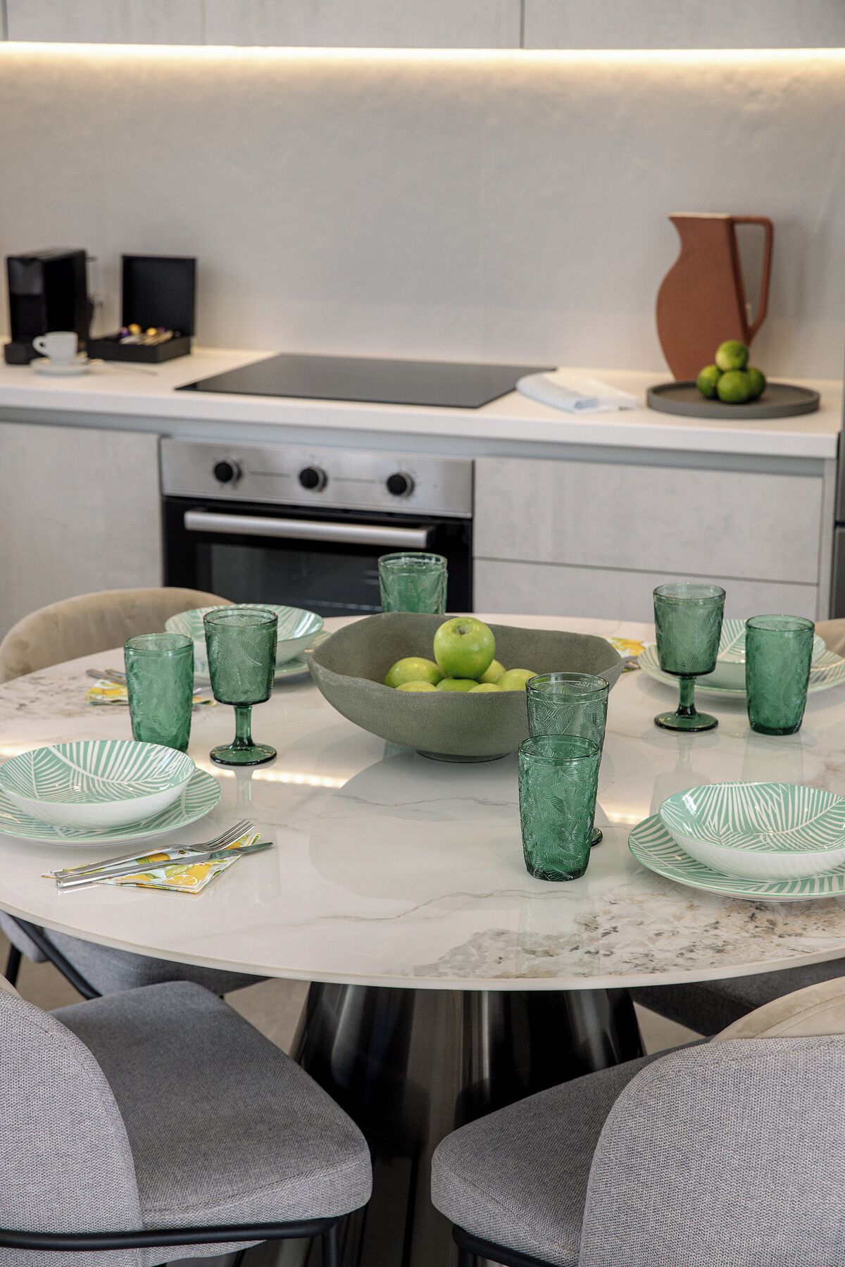 Una cocina moderna con una mesa redonda para cuatro personas, con vasos y platos verdes.