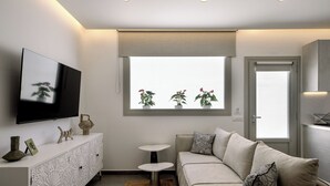 A modern living room with a sofa, TV, decorative items, and a window with plants. - Trinity Secret Villas (fira)
