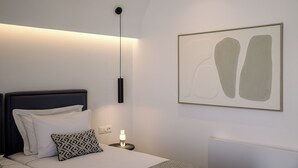 A modern bedroom with a bed, bedside lamp, and abstract artwork. - Trinity Secret Villas (fira)