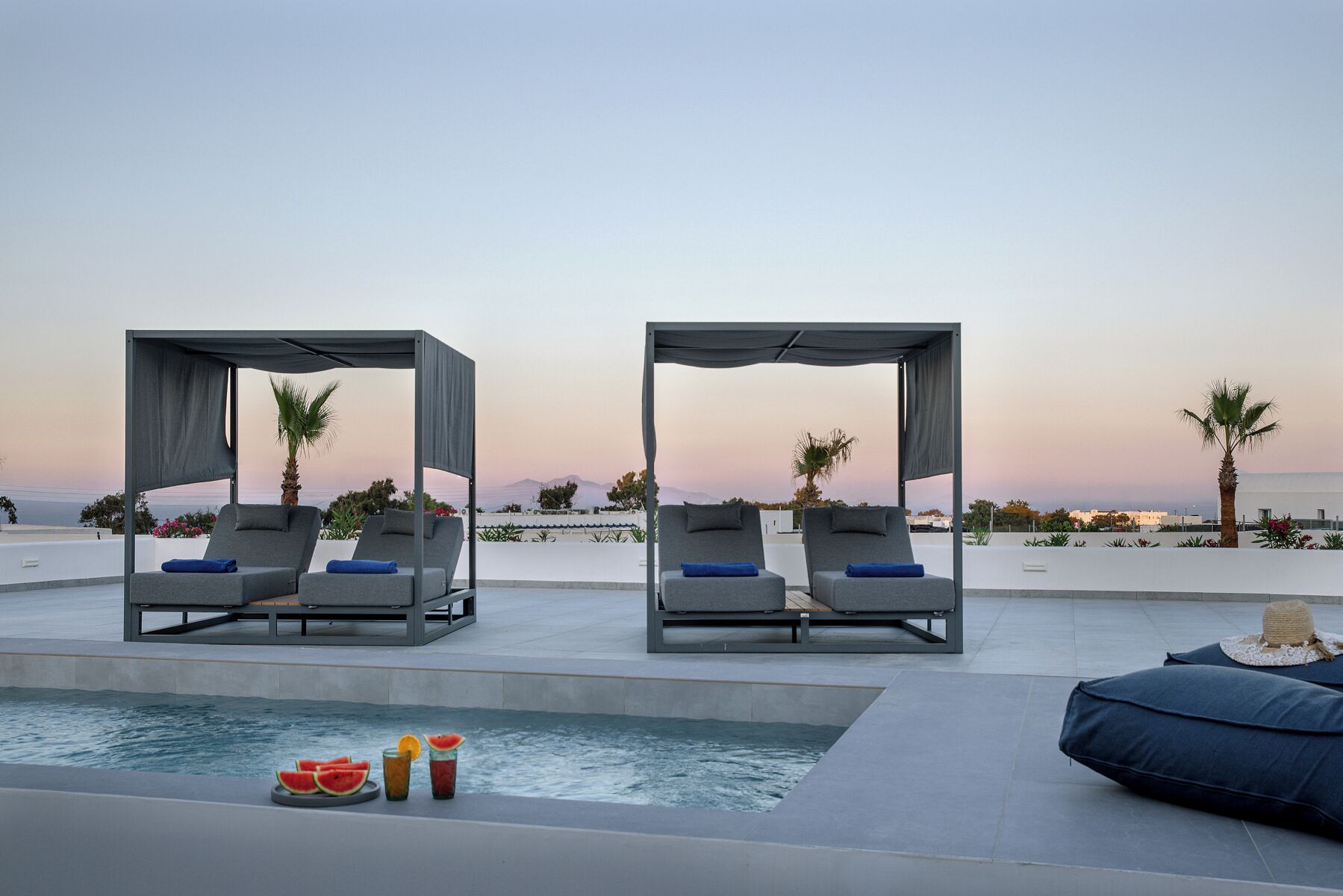 A poolside area with two lounge chairs under a canopy, a small pool, and a view of the sea.