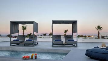 A poolside area with two lounge chairs under a canopy, a small pool, and a view of the sea.