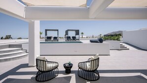 A rooftop terrace with a pool, two lounge chairs, a small table, and a pergola providing shade. - Trinity Secret Villas (fira)
