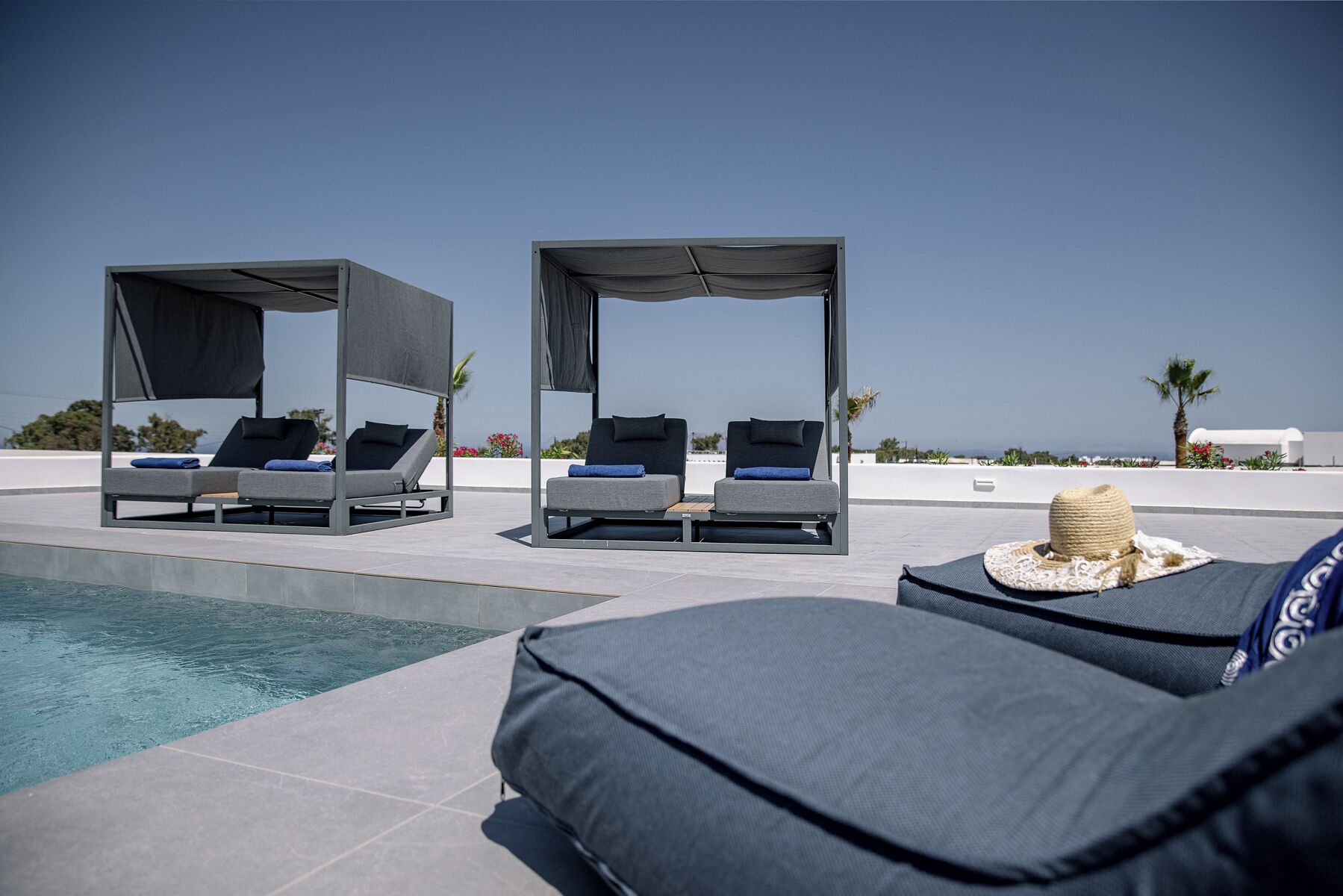A poolside area with lounge chairs and a covered seating area, overlooking a clear sky and distant landscape.