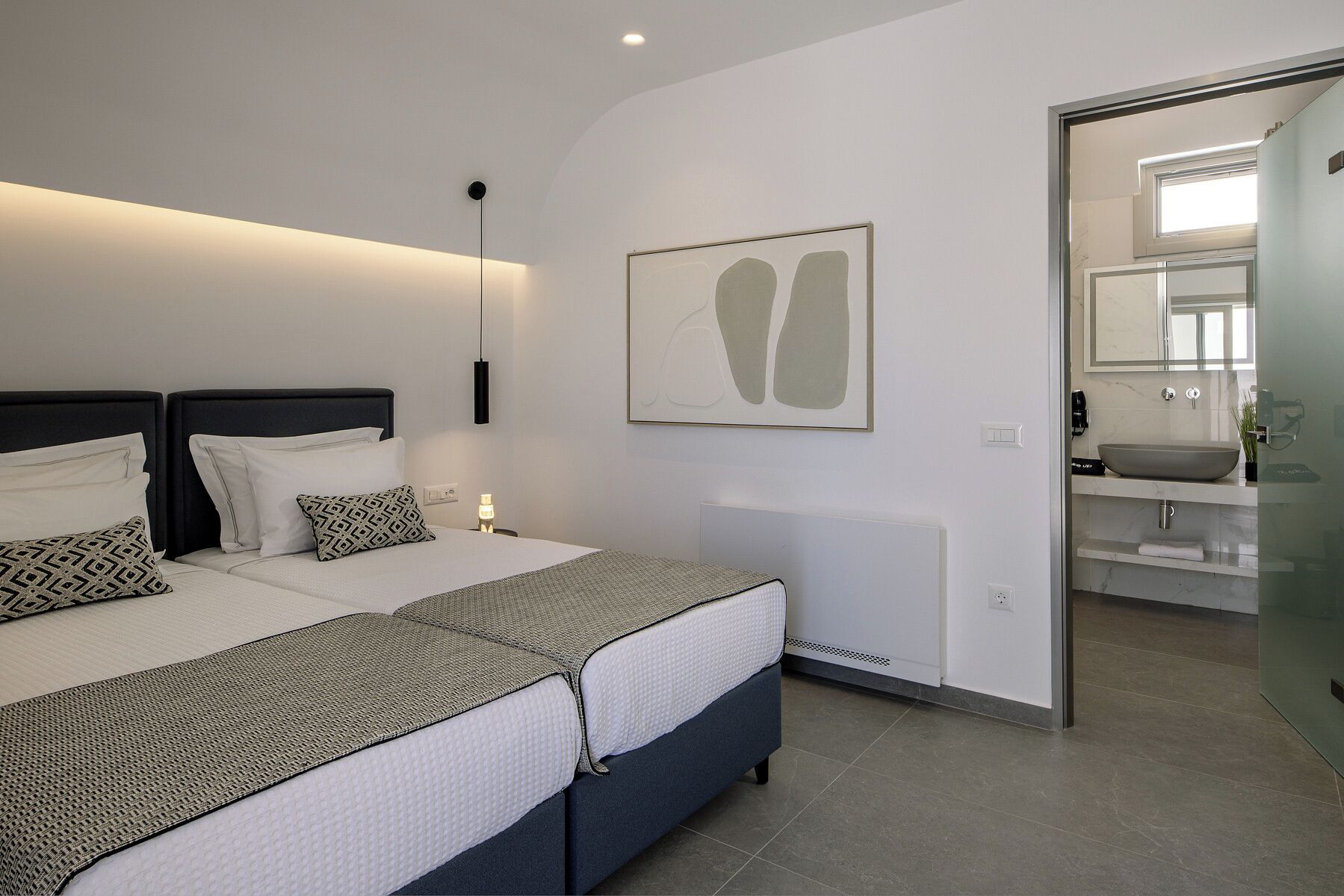 Ein modernes Schlafzimmer mit einem großen Bett, Nachttischen, einem Wandbild und einem durchgegangenen Türspalte erkennbaren Badezimmer.
