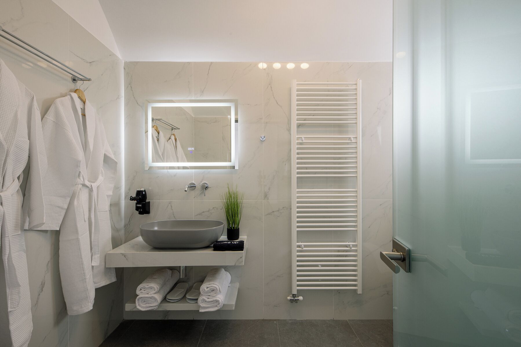 A modern bathroom with a marble sink, towel rack, and a glass shower enclosure.
