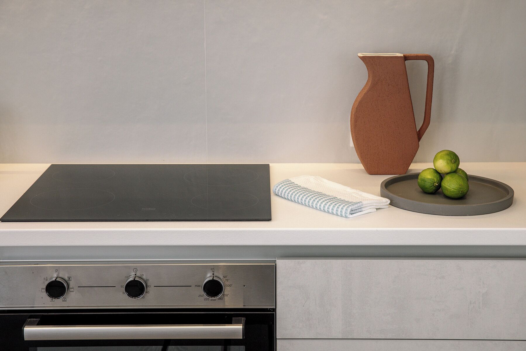 Une cuisine avec une planche à découper noire, un pichet marron et des citrons verts disposés sur un plateau.