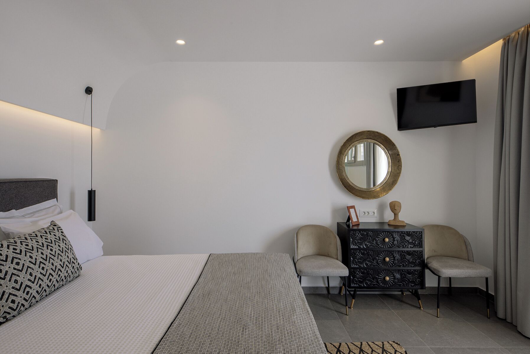 A modern bedroom with a bed, bedside table, chair, and a TV mounted on the wall.