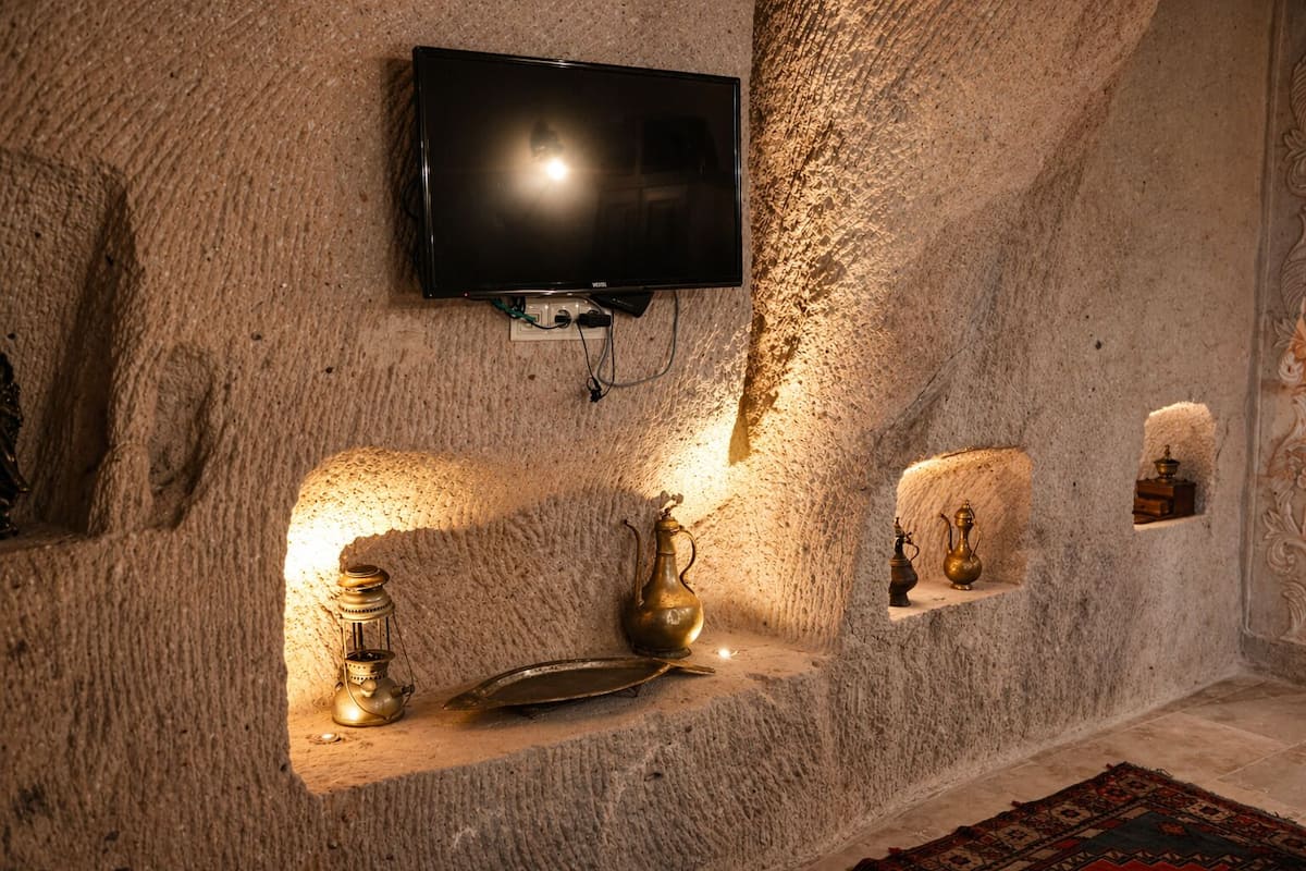 Ein Zimmer mit einem an der Wand befestigten Fernseher, einer kleinen Ablage mit Dekoration und einem Teppich mit Muster.