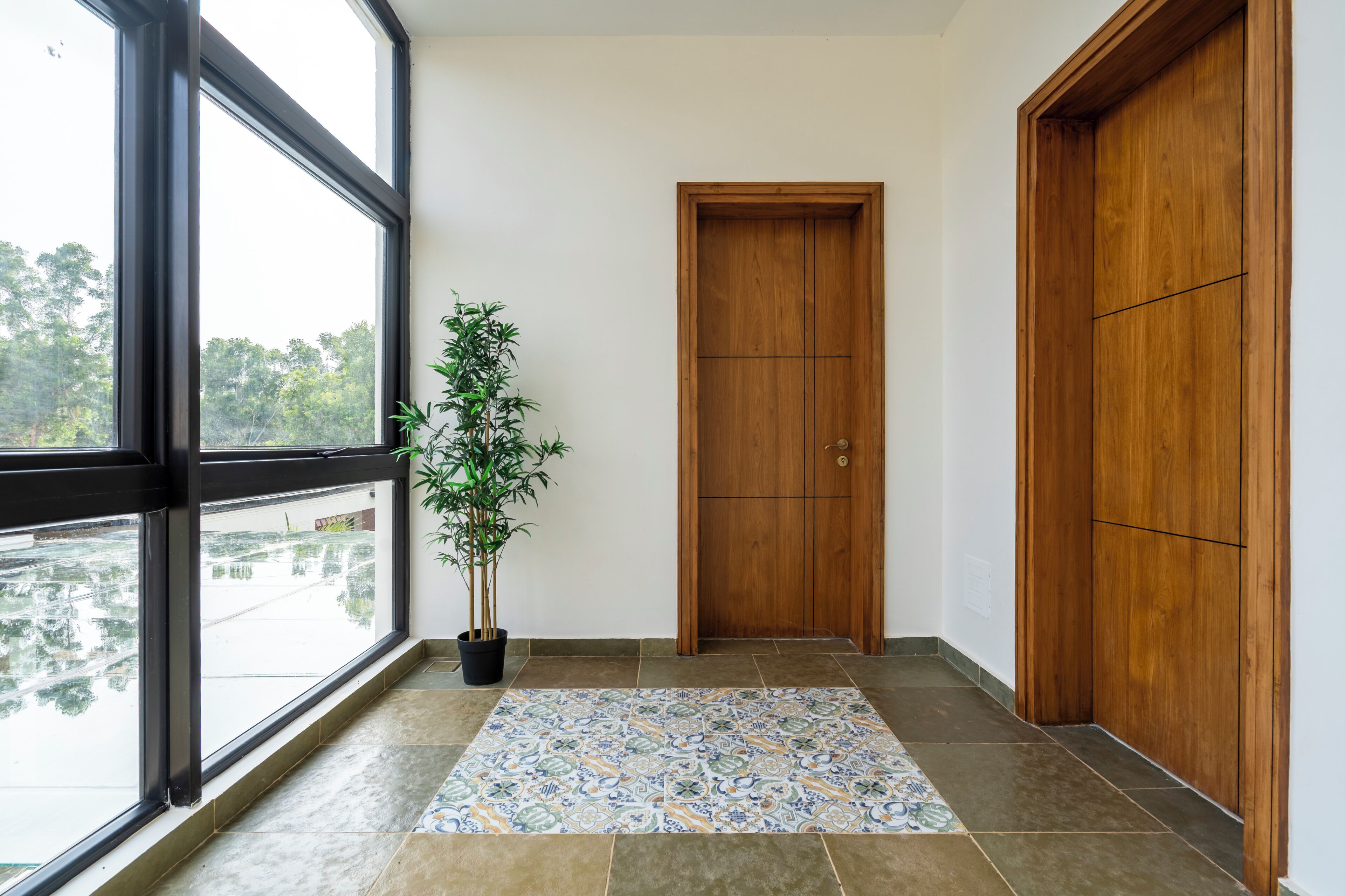 A hallway with a large window, a wooden door, and a tiled floor.