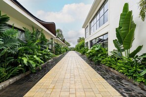 Uma passagem ladeada por vegetação exuberante e edifícios modernos com grandes janelas.