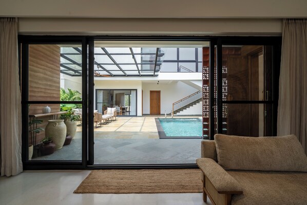 A modern interior with a sliding glass door leading to a pool area, a sofa, and a staircase.