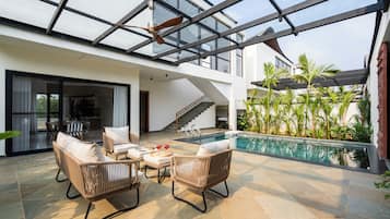 Un espacio moderno al aire libre con piscina, mobiliario de mimbre y techo de vidrio.