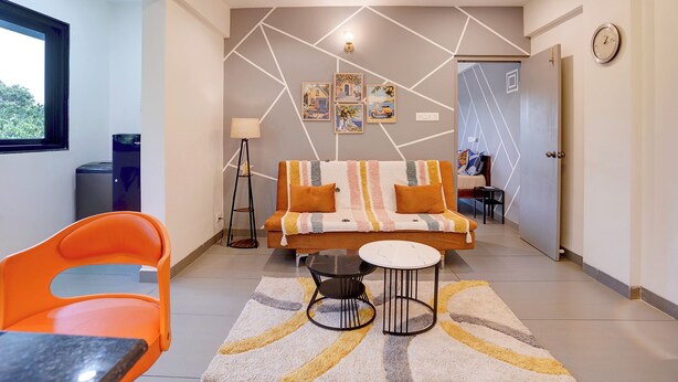 Uma sala de estar moderna com um sofá, uma mesa de centro e uma poltrona. Há uma luminária, um relógio e obras de arte na parede.