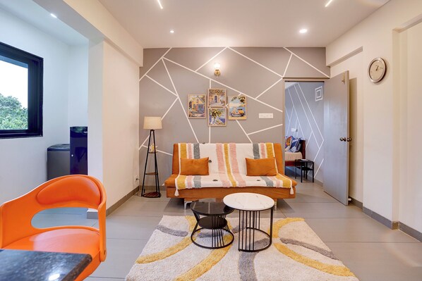 A modern living room with a sofa, a coffee table, and a chair. There is a lamp, a clock, and artwork on the wall. - FabHotel Casa Mandrem (Mandrem)