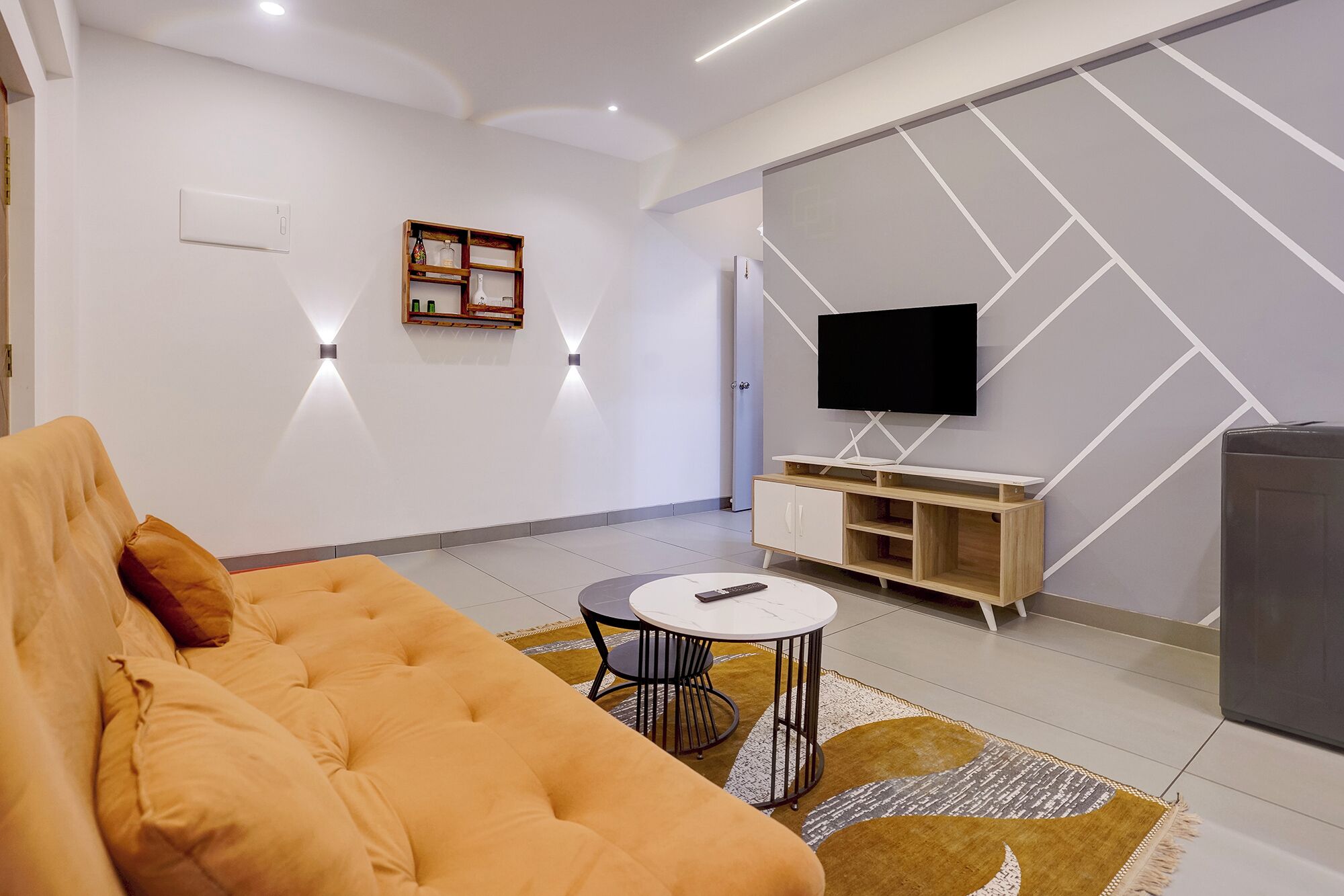 Una sala moderna con un sofá, una pequeña mesa redonda, un televisor montado en la pared y un mueble debajo.