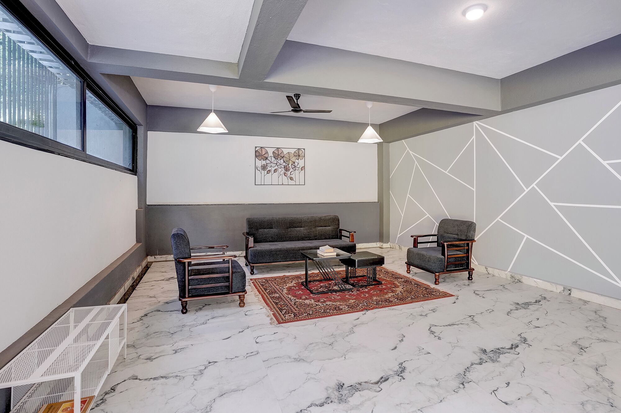 Una sala de estar moderna con un sofá gris, dos sillones, una mesa de centro y un tapete estampado rojo.