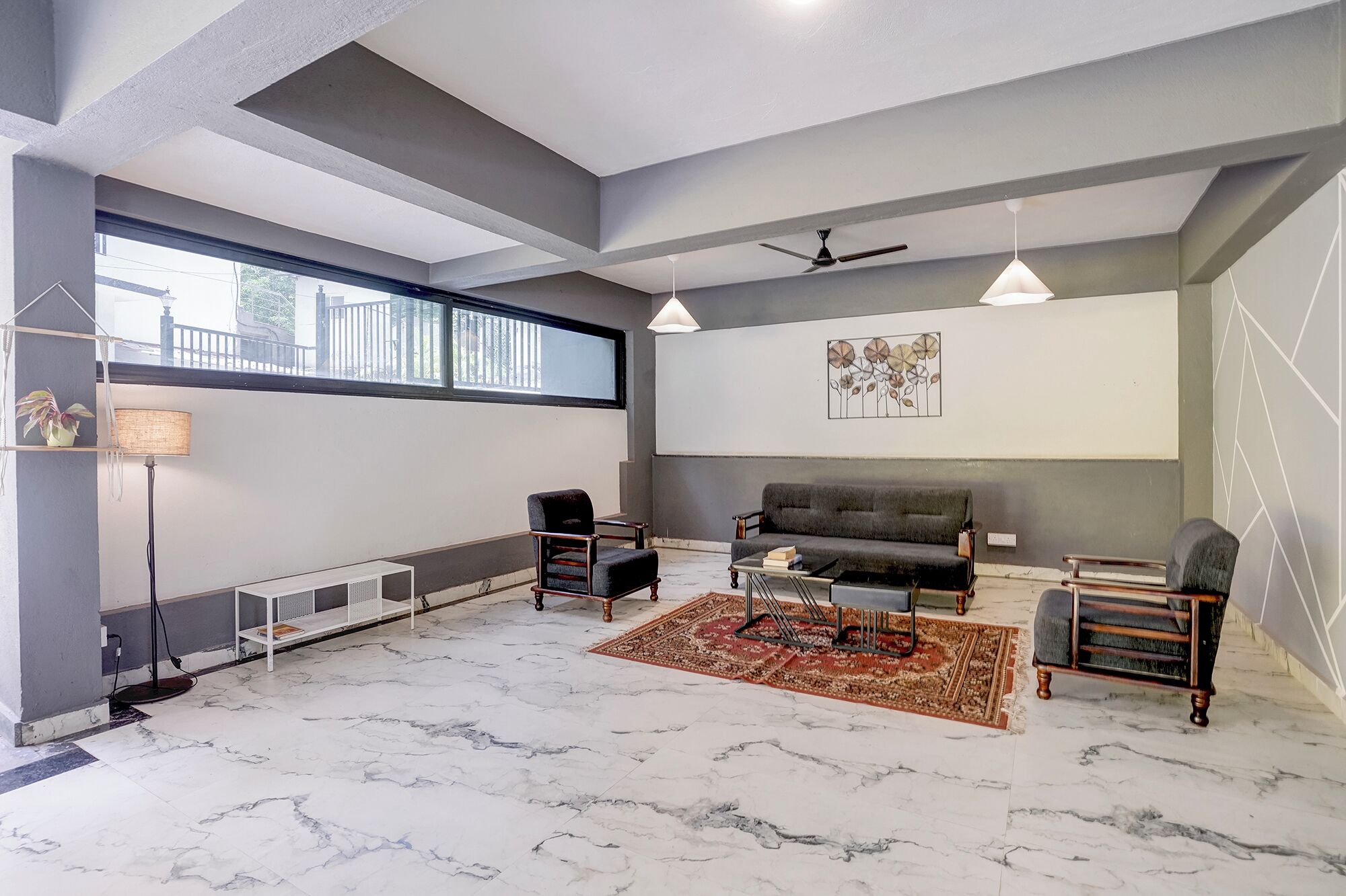 Una sala moderna con un sofá gris, dos sillones, una mesa de centro, una lámpara de pie y un ventilador de techo.