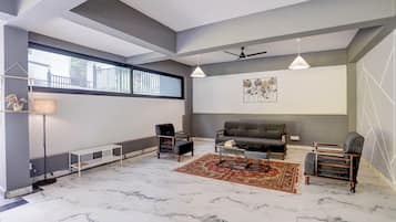 Una sala moderna con un sofá gris, dos sillones, una mesa de centro, una lámpara de pie y un ventilador de techo.