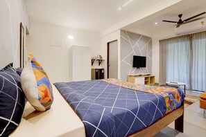Habitación de hotel con cama, televisor, escritorio y ventilador de techo.