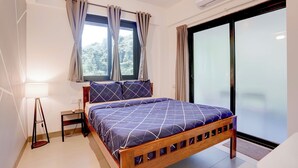 Quarto com uma cama, mesa de cabeceira, abajur, janela com cortinas e porta de correr de vidro.