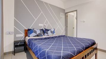 A bedroom with a bed, a nightstand, a wall-mounted power outlet, and a door.