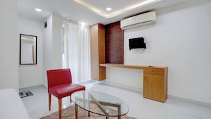 A modern room with a glass table, a red chair, a wooden cabinet, and an air conditioning unit. - Fabhotel Mv Luxury Rooms (Hyderabad)