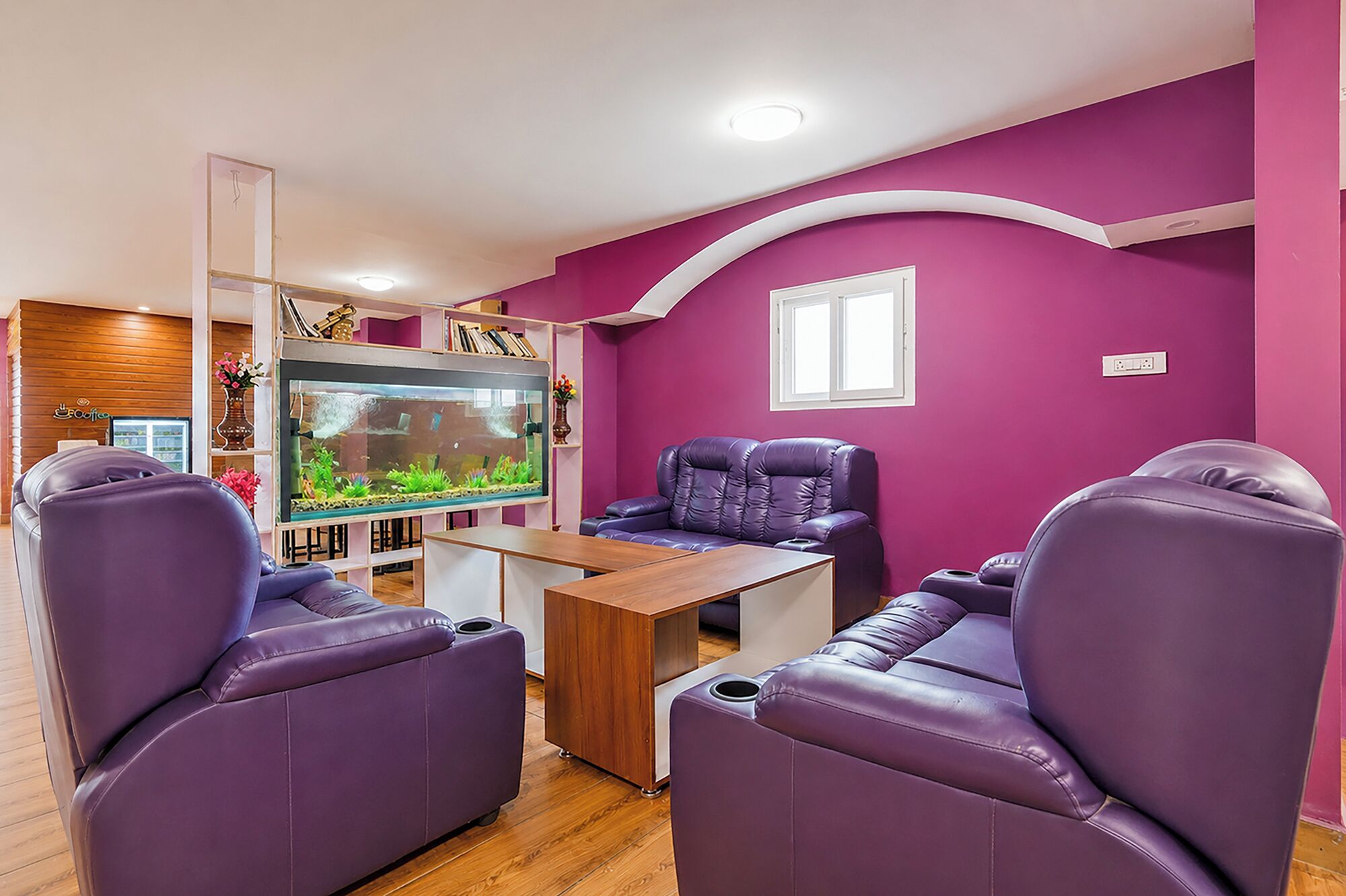 A living room with purple leather sofas, a wooden coffee table, and a large fish tank.