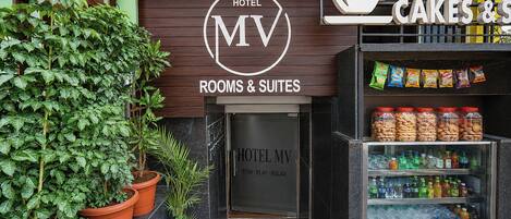 Entrada de un hotel con un cartel que dice 'Hotel MV Rooms & Suites' y una tienda de 'Cakes & Sweets'.